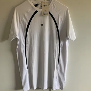 Vit T-shirt från MP - Säljer en vit T-shirt från MP i storlek S. Den har en stilren design med svarta detaljer längs sidorna. Perfekt för träning eller vardagsbruk. Materialet känns lätt och bekvämt, vilket gör den idealisk för sommar och vår. T-shirten är i nyskick och kommer i originalförpackning. Nypris 379kr
