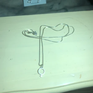 Silverhalsband med kvinnosymbol - Snyggt och stilrent silverhalsband med en kvinnosymbol som hänge. Perfekt för att bära till vardags eller som en subtil statement-piece. Kedjan är tunn och elegant, vilket gör den lätt att matcha med andra smycken. Ett måste för den som vill ha något unikt och meningsfullt.