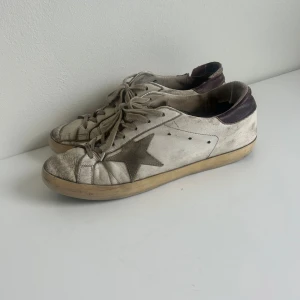 Golden goose skor - Säljer ett par vita sneakers från GGDB med en cool stjärndetalj på sidan. Skorna är välanvända med en vintage look och har snörning. Perfekta för en avslappnad stil och passar till det mesta i garderoben.
