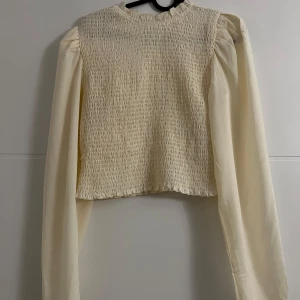 Långärmad blus  - Långärmad blus i nyskick. Fina detaljer i axlarna och en knapp baktill. Passar M/L. Mer cremefärgad än beige. 