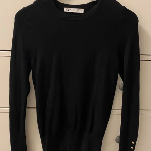 Svart tröja från Zara med guldknappar - Svart tunn finstickad top/tröja Zara stl M, fin detalj med guldknappar vid ärmslut. Liten i stl.