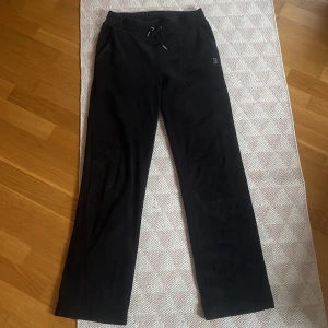 Svarta mjukisbyxor från Juicy Couture - Snygga svarta mjukisbyxor från Juicy Couture med glittrande text på baksidan. Byxorna har en bekväm passform med dragsko i midjan för justerbarhet. Perfekta för en avslappnad stil.