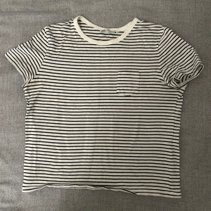 Randig t-shirt från Zara - Säljer en stilren randig t-shirt från Zara i svart och vit. Den har en liten bröstficka och korta ärmar. Perfekt för en avslappnad look.