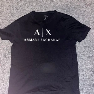 Svart t-shirt från Armani Exchange - Snygg svart t-shirt från Armani Exchange med deras logga tryckt på framsidan. Perfekt för en stilren look. Tillverkad i mjukt material för extra komfort. Liten i storleken