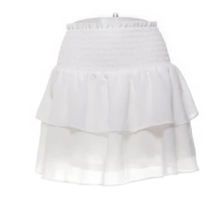 Vit volangkjol från Made by Chelsea - Säljer en söt vit kjol från Made by Chelsea med volanger och elastisk midja. Perfekt för en somrig look. Kjolen är kort och har en luftig design som ger en skön känsla. Passar bra till både sneakers och sandaler.