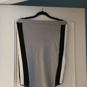 Grå kjol med svarta och vita detaljer från Lindex - Snygg grå kjol från Lindex med kontrasterande svarta och vita paneler på sidorna. Kjolen har en stilren design och är perfekt för en chic look. Den är tillverkad i ett mjukt och bekvämt material.