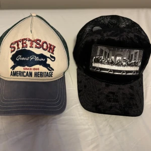 Keps från Stetson och en från hatstore - Två kepsar till salu. Den första är en Stetson-keps i beige och blått med texten 'American Heritage' och en buffel. Den andra kepsen är svart med ett tryck av 'Nattvarden'. Båda kepsarna har nätmaterial på baksidan för ventilation. Säljer 1 för 200 och båda för 350