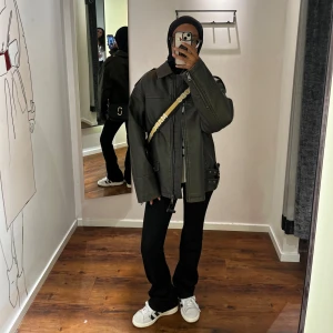 Grön skinnjacka med dragkedja - Snygg grön skinnjacka med dragkedja och krage. Jackan har en oversized passform och långa ärmar. Perfekt för en cool och avslappnad stil. Bilderna är tagna i provrummet innan jag köpte den. Inte använd!! Köpt för 1000kr.