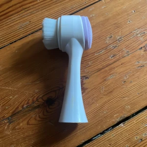 ansiktsborste - Praktisk dubbelverkande ansiktsborste med ett handtag i vitt. Ena sidan har mjuka borst för rengöring och den andra sidan har en silikonborste för exfoliering. Perfekt för daglig hudvårdsrutin.