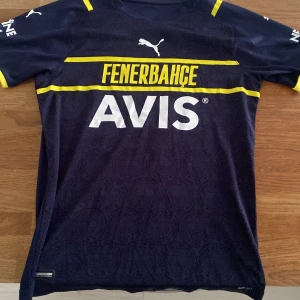  Fenerbahçe fotbollströja ”özil” - Snygg mörkblå Fenerbahçe fotbollströja från Puma med gula detaljer och sponsorloggor. Tröjan har korta ärmar och ett subtilt mönster med klubbens emblem. Nummer 10 och namnet Özil pryder ryggen. Perfekt för fans av klubben!