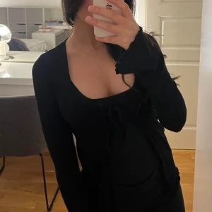 Svart långärmad topp från Bik Bok - Snygg svart långärmad topp från Bik Bok i storlek XS. Toppen har en v-ringad design med knytning framtill och är tillverkad i ett stretchigt material. Perfekt för en stilren look.