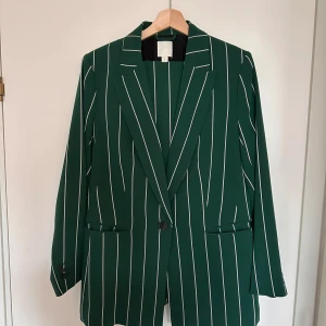 Grön randig kostym - Snygg grön kostym med vita ränder från H&M. Kavajen har en klassisk passform med knappar framtill och byxorna har en rak siluett. Perfekt för en stilren look.