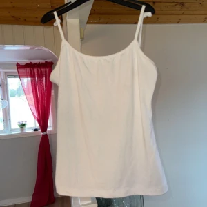 Vit linnetopp - Säljer en enkel och stilren vit linnetopp med smala axelband. Perfekt för varma sommardagar eller som ett basplagg i garderoben. Stor i storleken därför jag har knutit på axelbandet 