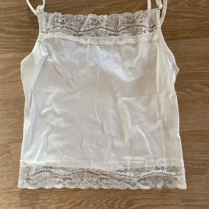 Vit linne med spetsdetaljer - Säljer ett sött vit linne med smala justerbara axelband och vacker spetsdetalj både upptill och nedtill.  Stryks och tvättas innan det skickas.