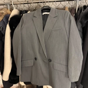 Grå kavaj från primark - Snygg grå kavaj från primark-London med klassisk design. Den har två knappar framtill och fickor med lock. Perfekt för en stilren look.