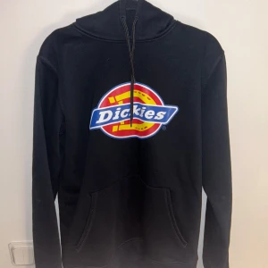 Svart hoodie från Dickies - Säljer en svart hoodie från Dickies med deras ikoniska logga i rött, gult och blått på bröstet. Helt ny, aldrig använd