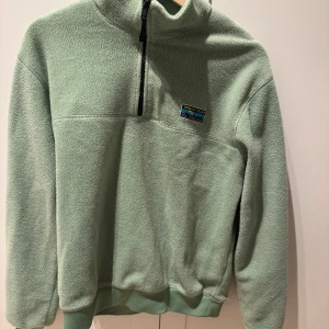 Grön fleece tröja från Patagonia - Mysig grön fleece tröja från Patagonia med halv dragkedja och hög krage. Perfekt för kyliga dagar!