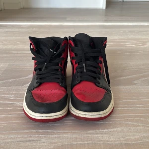 Svart och röd Nike Air Jordans - Snygga Nike Air Jordans i svart och rött med klassisk snörning. Skorna har en hög design och den ikoniska Nike-loggan på sidan. Perfekta för dig som vill ha en stilren och sportig look.