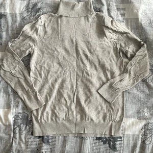 Beige polotröja från H&M - Säljer en stilren beige polotröja med långa ärmar. Perfekt för kyligare dagar och enkel att matcha med olika outfits. Tröjan har en klassisk design med ribbstickade muddar vid ärmslut och nederkant. Lite strynklig men det ordnar sig med att stryka det bara en gång. 