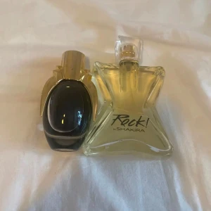 Parfymflaskor från Shakira och okänt märke - Två parfymflaskor, en från Shakira med namnet 'Rock!' i en stjärnformad flaska med gul vätska. Den andra flaskan är oval med en mörk vätska och guldfärgad kork. Märket är lady gaga. Båda för 200kr