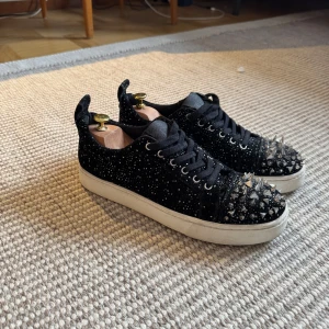 Steve madden 44 - Snygga svarta sneakers med glittrig yta och coola nitar på tån. Skorna har snörning och en vit sula som ger en skarp kontrast. Perfekta för att göra din event outfit lite roligare:) 