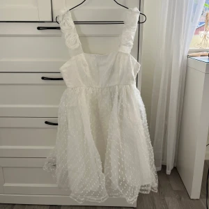 Vit prickig klänning med volangdetaljer - Vit klänning med prickigt mönster och volangdetaljer på axelbanden. Klänningen har en luftig passform och är perfekt för studenten/sommaren. Den är oanvänd🤗