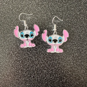 Söta örhängen med stitch  - Charmiga örhängen med en tecknad figur i rosa och blått. Perfekta för att lägga till en lekfull touch till din stil. De har en krok för enkel användning.