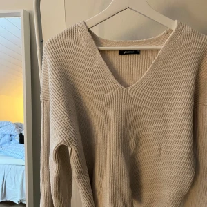 Beige stickad tröja från Gina Tricot - Säljer en stilren beige stickad tröja från Gina Tricot. Tröjan har en v-ringad design och långa ärmar, perfekt för kyligare dagar. 