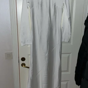 Vit långklänning - Elegant vit långklänning med långa ärmar. Perfekt för formella tillfällen med sin stilrena design och klassiska snitt.