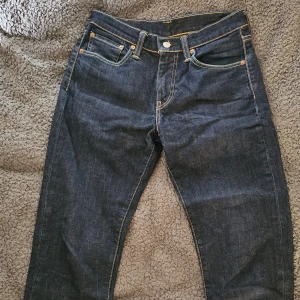 Levi's 511 jeans i mörkblå denim - Snygga Levi's 511 jeans i mörkblå denim med klassisk femficksdesign och gul kontrastsöm. Dessa jeans har en slim passform och är perfekta för en stilren look. Märkeslappen i läder sitter på baksidan av midjan.