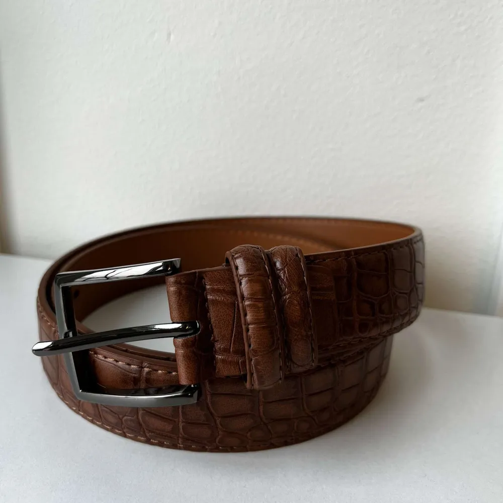 • 🐊 Äkta alligatorläder • 🇮🇹 Hantverksmässigt tillverkat i Italien • 🌱 Fairtrade & Etiskt framställt • ✨ Högkvalitativt spänne • 🤎 Elegant brun nyans • 👌 Perfekt passform • 🌍 Hållbar & miljövänlig produktion • 💎 Exklusiv accessoar • ⚡ Begränsad upplaga. Asusteet.