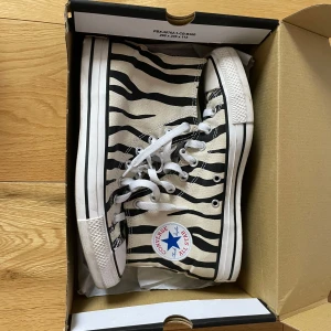 Zebramönstrade Converse All Star - Säljer ett par coola zebramönstrade Converse All Star sneakers. Skorna har en klassisk hög modell med snörning och den ikoniska Converse-loggan på sidan. Perfekta för att ge din outfit en unik touch! ENDAST ANVÄNDA EN GÅNG! Säljs med original kartong 