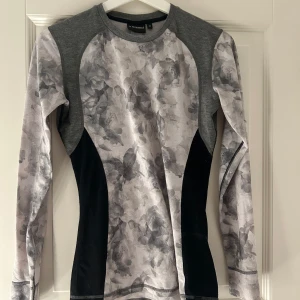 Grå blommig underställströja från Everest - Säljer en snygg grå underställströja från Everest med blommigt mönster. Tröjan har långa ärmar och en rund halsringning. Den är använd mycket men är fortfarande fin.