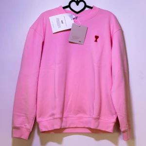 Rosa sweatshirt från Ami Paris - Säljer en helt ny rosa sweatshirt från Ami med ett litet rött hjärta broderat på bröstet. Tröjan har en klassisk rund halsringning. Perfekt för en avslappnad stil. Passar tjejer i storlek M, kom med bud och frågor!🤗