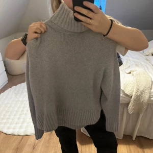 Grå kashmir polotröja - Säljer en supermjuk och stilren grå polotröja från Zara i kashmir. Perfekt för kyliga dagar med sin höga krage och långa ärmar. Tröjan har en ribbad design vid krage, ärmslut och nederkant. Ett måste i garderoben för en elegant look!