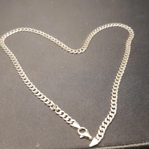 Riktigt silver halsband - Snyggt silverfärgat halsband med en robust karbinhake. Kedjan har en klassisk design med platta länkar som ger en stilren look. Perfekt för att komplettera din outfit med en touch av elegans.