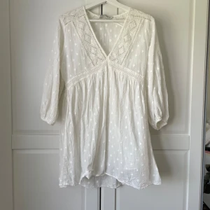 Vit blommig klänning med spetsdetaljer - Säljer en superfin vit klänning med prickigt mönster med v-ringning. Den har trekvartsärmar och en lös passform som är perfekt för sommardagar. Klänningen är köpt för över två år sedan, men är använd runt två tre gånger. Passar till bla. studenten och konfitmation 🥰