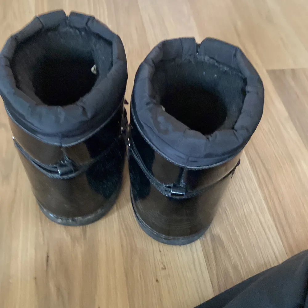 Säljer ett par svarta moon boots i syntetmaterial. De är perfekta för vintern med sin varma och vadderade insida. Skorna har snörning framtill och en glansig yta som ger dem en cool look. Perfekta för kalla dagar!. Skor.