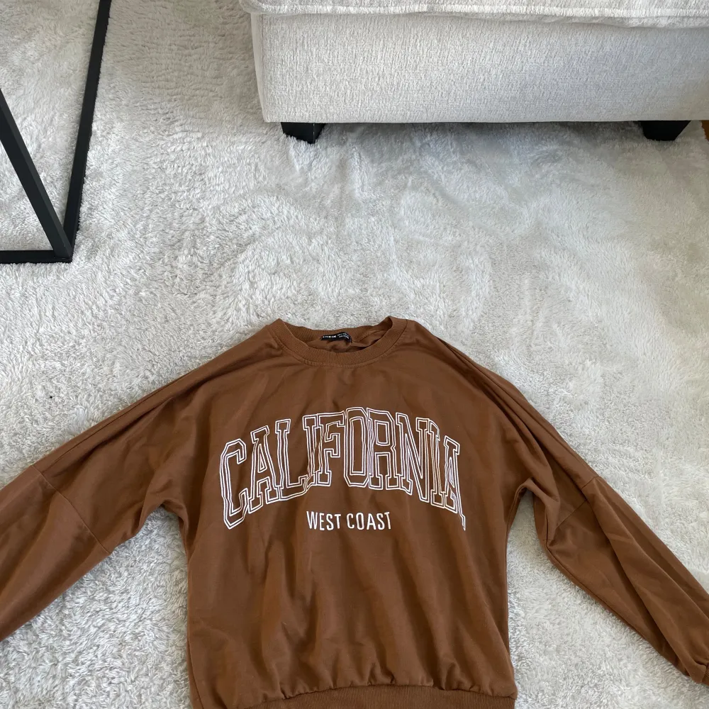 Säljer en brun sweatshirt från Shein med texten 'California West Coast' tryckt på framsidan. Tröjan har långa ärmar och är gjord i ett mjukt material. Perfekt för en avslappnad stil!. Tröjor & Koftor.