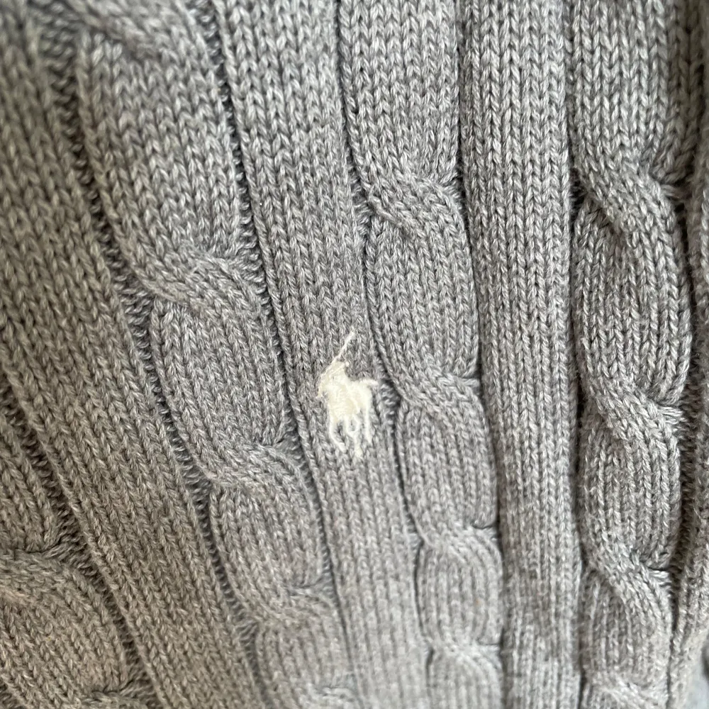 Säljer en snygg och klassisk grå stickad tröja från Ralph Lauren. Den har ett diskret kabelstickat mönster och en liten broderad logga på bröstet. Perfekt för höst och vinter, med långa ärmar och en bekväm passform. Passar både till vardags och lite finare tillfällen.. Tröjor & Koftor.