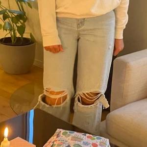 Högmidjade jeans med vida ben - Jättesnygga jeans med hål över knäna. Lite slitna längst ner och har knappt märkbar fläck på ena bakfickan. Har gått lite sönder vid gylfen som syns på sista bilden. Hör av er vid frågor! Köparen står för frakten