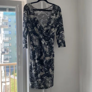 Mönstrad klänning med trekvartsärm - Säljer en snygg mönstrad klänning med trekvartsärm. Den har en omlott-design och en v-ringad hals. Perfekt för både vardag och fest!