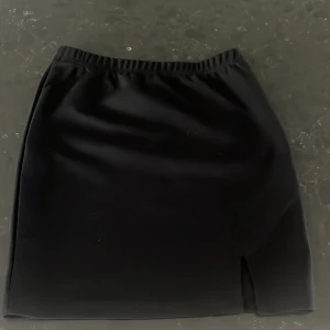 Svart kjol från Shein - Säljer en stilren svart kjol från Shein i storlek XS. Kjolen har en enkel design med en liten slits på sidan som ger den en extra touch. Perfekt för både vardag och fest! 🖤