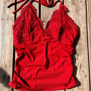 Vinröt spetslinne - ‼️OBS SISTA BILDEN HAR MER KORREKT FÄRG‼️ Säljer ett snyggt rött linne med spetsdetaljer. Toppen har en vacker blommig spets upptill och är ärmlös med knytband runt halsen. Perfekt för en somrig dag eller en festkväll!