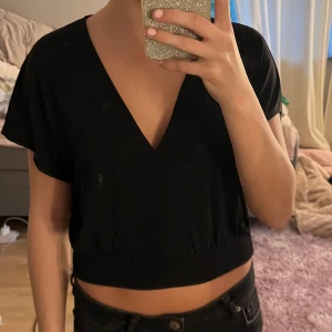 Svart croppad topp - Säljer en stilren svart croppad topp med v-ringning. Toppen har korta ärmar och är perfekt för en avslappnad men snygg look. Passar bra till både jeans och kjol!
