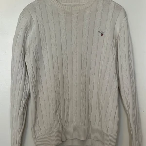 Vit stickad tröja från GANT - Säljer en snygg vit stickad tröja från GANT. Den har ett klassiskt kabelstickat mönster, Perfekt för höst och vinter.