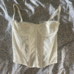 Vit spetskorsett - Säljer en superfin vit korsett med spetsdetaljer. Den har justerbara axelband och en snygg snörning i ryggen. Perfekt för fest eller en speciell kväll. Passar bra till både kjol och byxor! Använde den 1 gång 