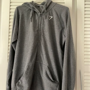 Gymshark zip-hoodie - En grå gymshark zip-hoodie i storlek L, herrstorlek🫶 bra kvalitet förutom fläckar på insidan av tröjan, men inget som märks av🥰  
