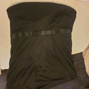 Svart axelbandslös klänning - Säljer en elegant svart axelbandslös tub topp med en söt rosett i midjan. Perfekt för festliga tillfällen! toppen är i bra skick och har en stilren design som passar till många olika tillfällen🖤