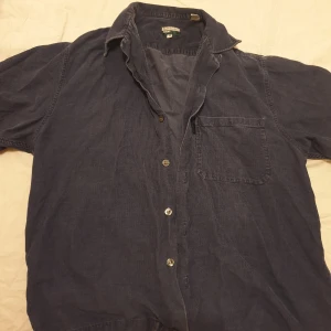 Skjorta  - En skjorta med långa ärmar och en ficka på bröstet. Knappar i metall. Säljs för 50